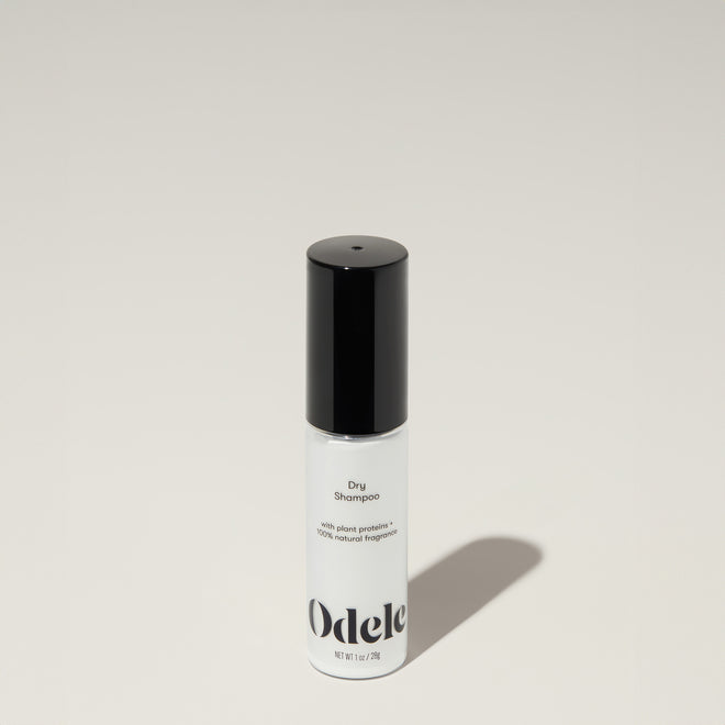 A bottle of Odele Dry Shampoo stands upright against a plain, light-colored backdrop with the front of the label facing the camera.