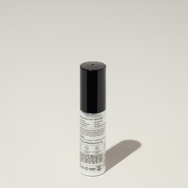 A bottle of Odele Dry Shampoo stands upright against a plain, light-colored backdrop with the back of the label facing the camera.