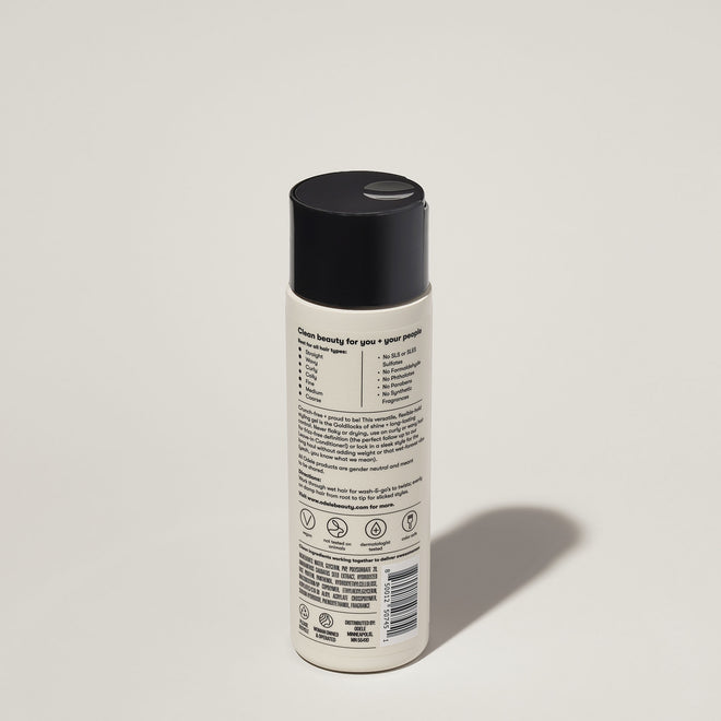 A bottle of Odele Flex Hair Gel stands upright against a plain, light-colored backdrop with the back of the label facing the camera.