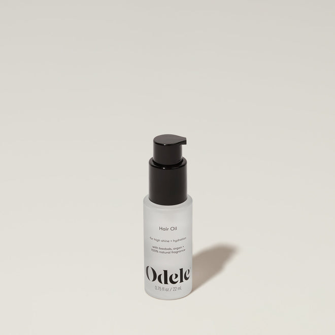 A bottle of Odele Hair Oil stands upright against a plain, light-colored backdrop with the front of the label facing the camera.