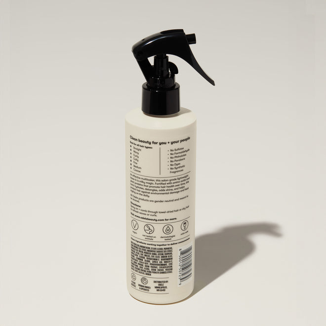 A bottle of Odele Leave-in Detangling Tonic stands upright against a plain, light-colored backdrop with the back of the label facing the camera.