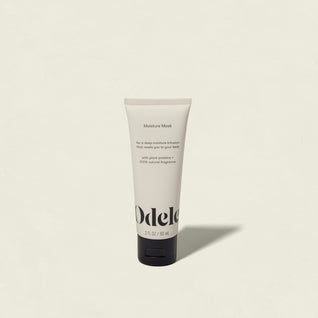 A 2 fl oz (60 ml) tube of Odele Moisture Mask Mini with argan and jojoba stands upright on a light background. The beige packaging, with black text and a black cap, emphasizes deep hydration benefits.