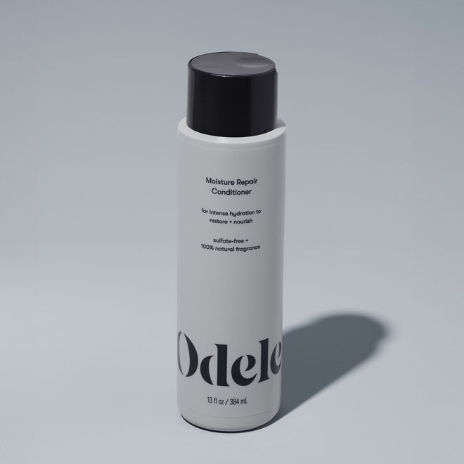 A bottle of Odele Moisture Repair Conditioner stands upright against a plain, light-colored backdrop with the front of the label facing the camera.