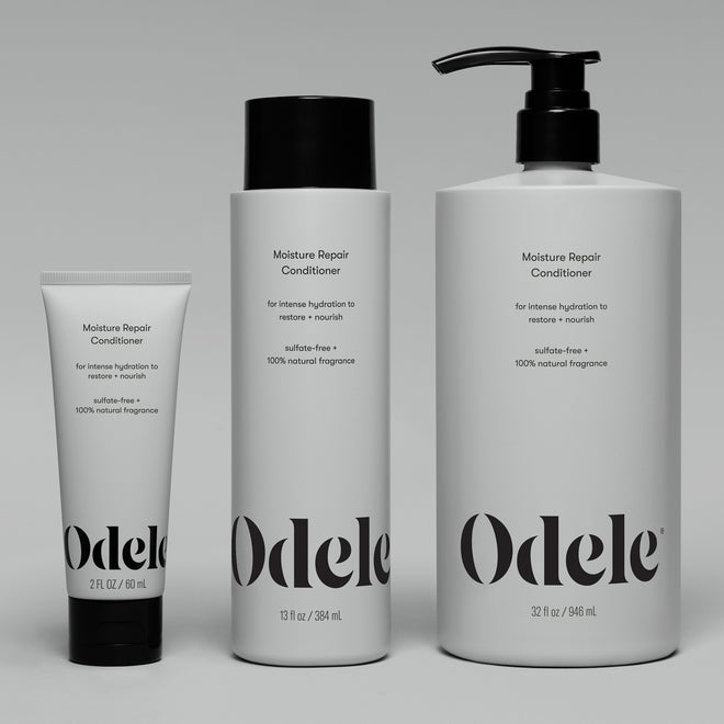 Three Odele Moisture Repair Conditioner bottles—including the Moisture Repair Conditioner Mini—are upright on a gray background. Their white packaging with black text highlights hydration benefits and color protection.