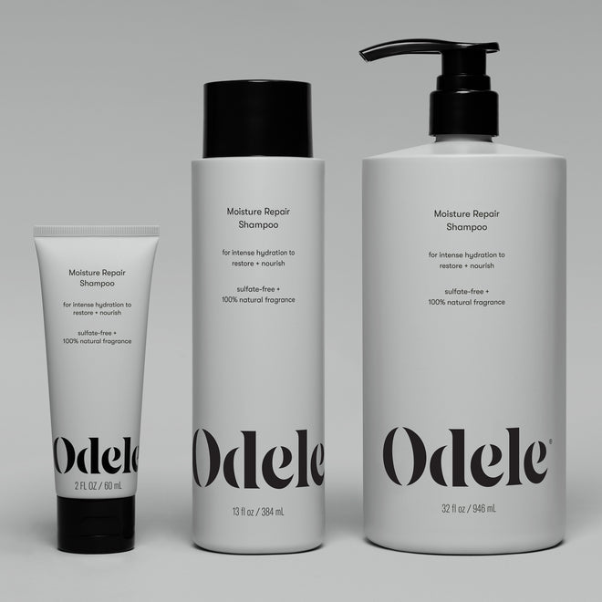 Three Odele Moisture Repair Shampoo Mini bottles (2 fl oz tube, 13 fl oz bottle, and 32 fl oz pump) are arranged side by side on a gray background, highlighting this salon-grade shampoo for intense hydration.