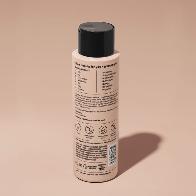 A bottle of Odele Moisturizing Body Wash stands upright against a plain, light orange backdrop with the back of the label facing the camera.