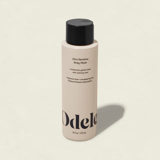 A beige bottle of Ultra Sensitive Body Wash with a black cap rests on a light surface. Its label highlights a gentle, fragrance-free formula and states it’s accepted by the National Eczema Association for sensitive skin.