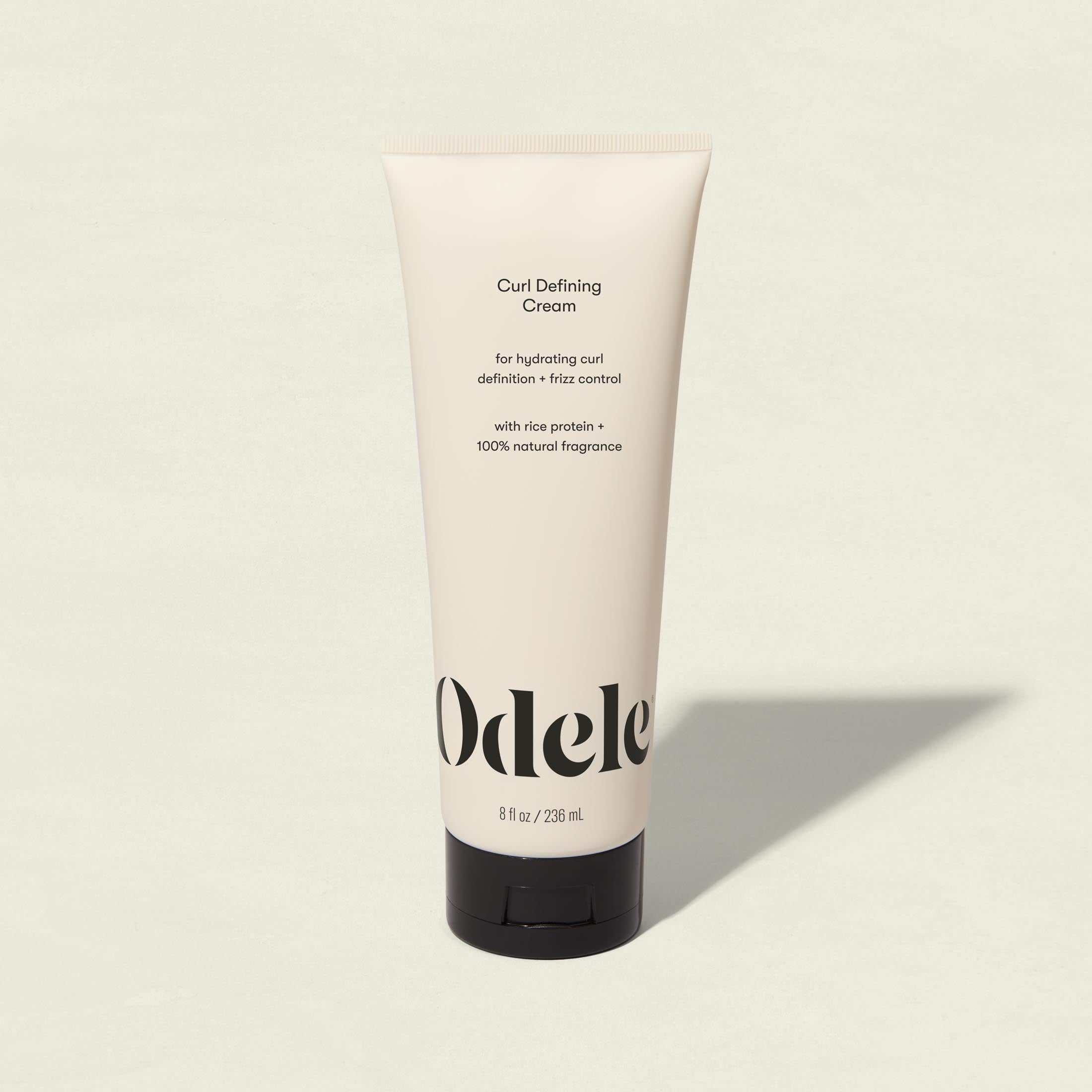 A beige tube of Curl Defining Cream stands upright on a light surface, featuring black text that highlights its hydrating, curl-defining, and frizz-control benefits for hair. The tube holds 8 fl oz (236 mL).