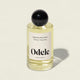 The Odele Signature Hair Scent, in a clear glass bottle with a black spherical cap and “Oakmoss / Ylang Ylang” label, is shown on a light beige background, suggesting fresh air with hints of cucumber and bamboo.