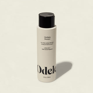 A white bottle of Clarifying Shampoo with a black cap and minimalist black branding on a light background. This sulfate-free formula gently cleanses, leaving hair refreshed and healthy.