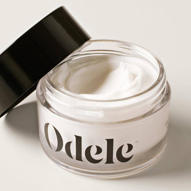An open jar of Odele Cream Pomade with a black lid leaning against the side contains smooth white pomade.