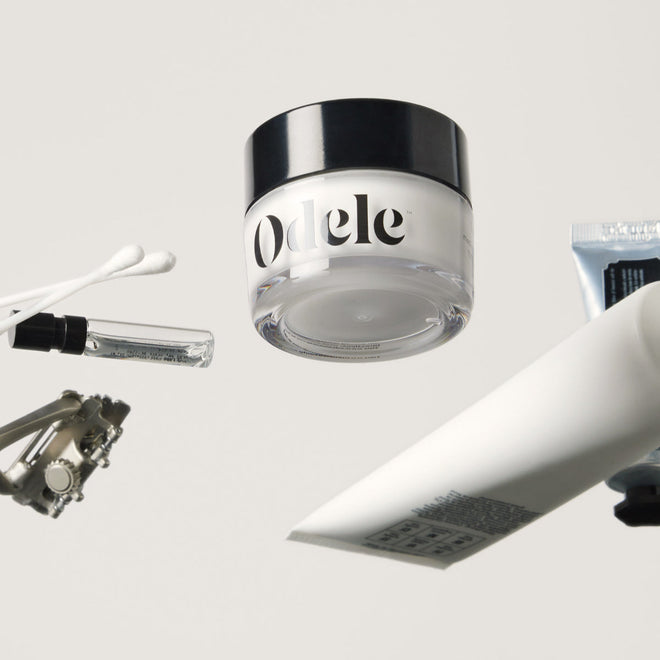 A jar of Odele Cream Pomade sits with an assortment of miscellaneous beauty items on a clear surface above the camera.