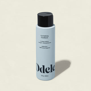 The Odele Curl Defining Conditioner—light blue with a black cap, minimal design, and black text—is displayed upright on a light beige background, ideal for deep moisture and healthy-looking curls.