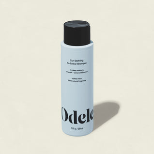 A light blue bottle of Curl Defining No-Lather Shampoo with a black cap and bold text stands upright on an off-white background—ideal for deep hydration and strengthening curls.