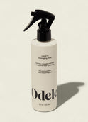 A white bottle of Odele Leave-in Detangling Tonic with a black spray nozzle stands upright on a light beige background. The label highlights plant proteins, natural fragrance, and heat protection for easy detangling.