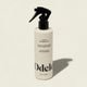 A white bottle of Odele Leave-in Detangling Tonic with a black spray nozzle stands upright on a light beige background. The label highlights plant proteins, natural fragrance, and heat protection for easy detangling.
