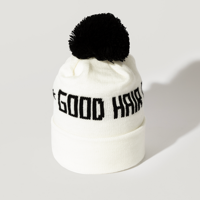 The Good Hair Day Winter Hat is a white knit beanie featuring a black pom-pom and GOOD HAIR in bold black text on the front. This limited-edition item is shown against a simple white background.