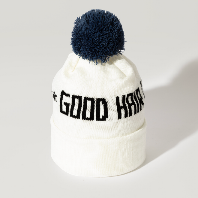The Good Hair Day Winter Hat is a white knit beanie with a dark blue pom-pom and GOOD HAIR in bold black letters on the front. This limited-edition hat is made in Minnesota for cozy comfort all winter.