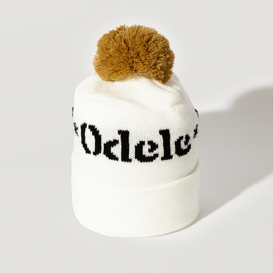 The Good Hair Day Winter Hat is a white knit beanie with a folded brim, black text, and a large brown pom-pom—expertly crafted for quality, comfort, and style.
