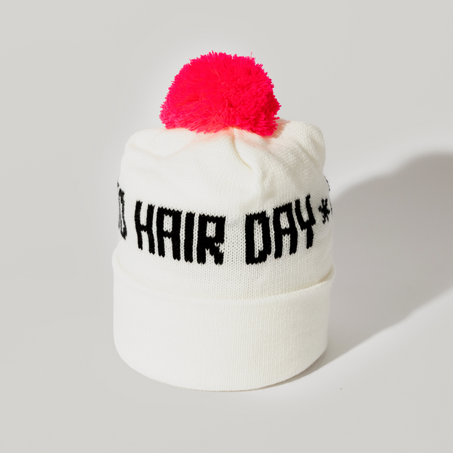 The Good Hair Day Winter Hat is a white knit beanie with a bright pink pom-pom and black HAIR DAY text on the front, designed for quality comfort by winter experts.