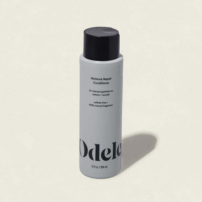 A white bottle of Moisture Repair Conditioner with a black cap and minimalist branding stands against a plain light background, highlighting its promise of intense hydration in a salon-grade formula.
