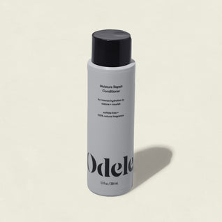 A white bottle of Moisture Repair Conditioner with a black cap and minimalist branding stands against a plain light background, highlighting its promise of intense hydration in a salon-grade formula.