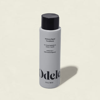 A white bottle of Moisture Repair Conditioner with a black cap and minimalist branding stands against a plain light background, highlighting its promise of intense hydration in a salon-grade formula.