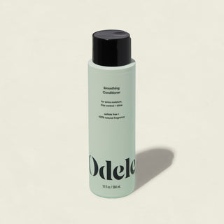 A light green bottle of Smoothing Conditioner with a black cap features text for extra moisture and frizz control. Sulfate-free with a natural fragrance, this conditioner enhances shine. The bottle is shown on a plain background.
