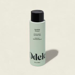 A light green bottle of Smoothing Shampoo with a black cap and minimalist branding on the front offers frizz control and shine, set against a plain, light background.