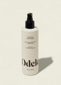 A white bottle of Odele Texturizing Sea Salt Spray with a black nozzle and minimalist label sits on a light background, casting a shadow to the right—ideal for creating effortless, tousled texture and that signature beach hair look.