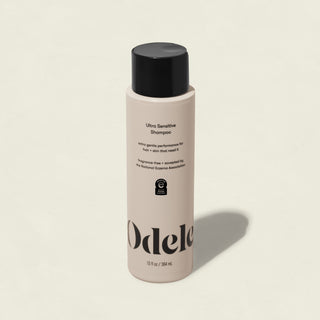 A beige bottle of Odele Ultra Sensitive Shampoo stands upright on a light background. The salon-grade shampoo, in black-capped packaging, displays sleek black text and the logo—ideal for sensitive skin and eczema-prone scalps.