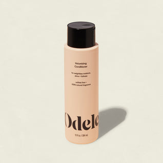 A Volumizing Conditioner in a peach bottle with a black cap and bold black text on a simple background provides weightless moisture to boost hair strength.