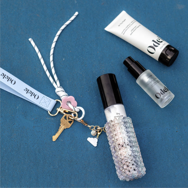 The Touch-Ups To Go Bundle, featuring two Ode bottles, a decorative spray bottle, an Air Dry Styler Mini, a keychain with keys, and a lanyard, is arranged on a blue surface for effortless hair and skincare.