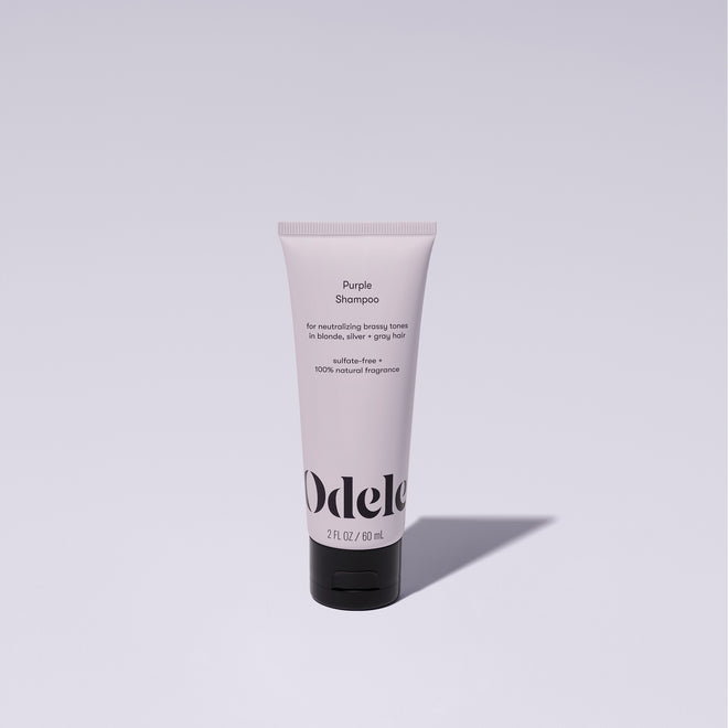A bottle of Odele Purple Shampoo stands upright against a plain, light-colored backdrop with the front of the label facing the camera.