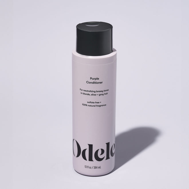 A bottle of Odele Purple Conditioner stands upright against a plain, light-colored backdrop with the front of the label facing the camera.