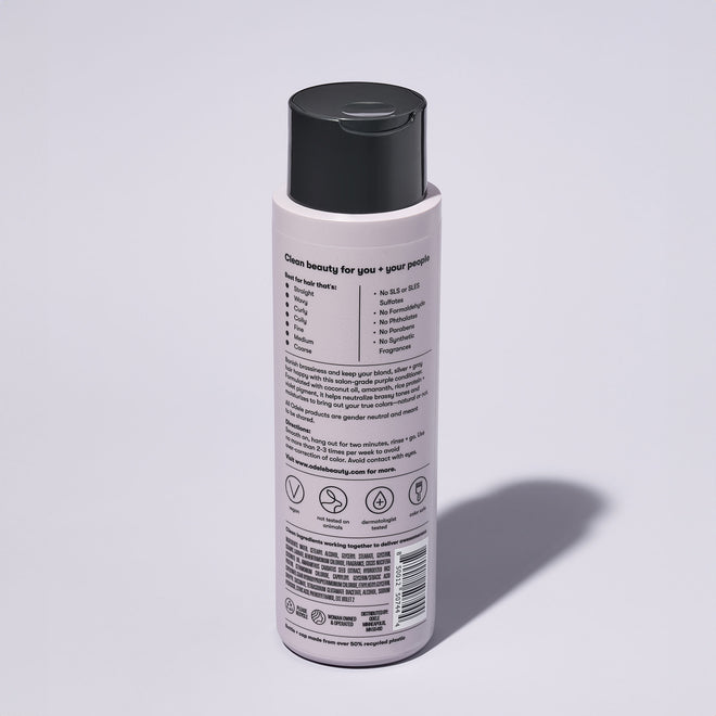 A bottle of Odele Purple Conditioner stands upright against a plain, light-colored backdrop with the back of the label facing the camera.