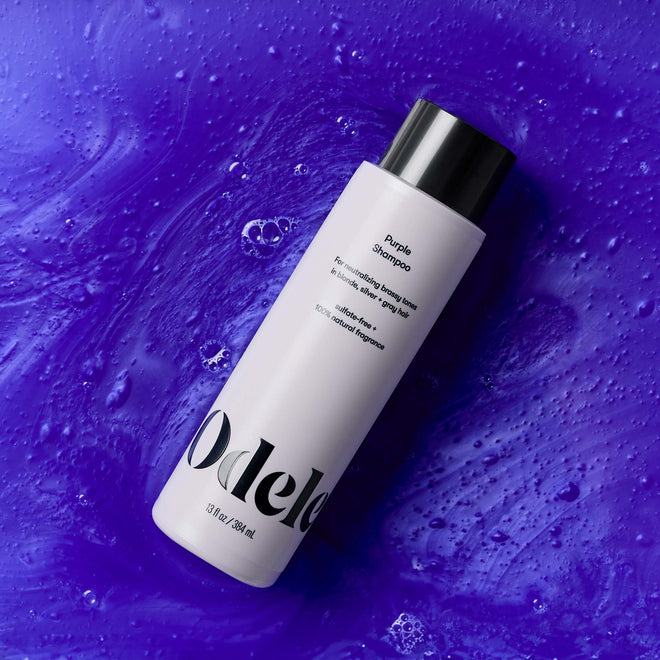 A bottle of Odele Purple Shampoo lays in a pool of purple shampoo.