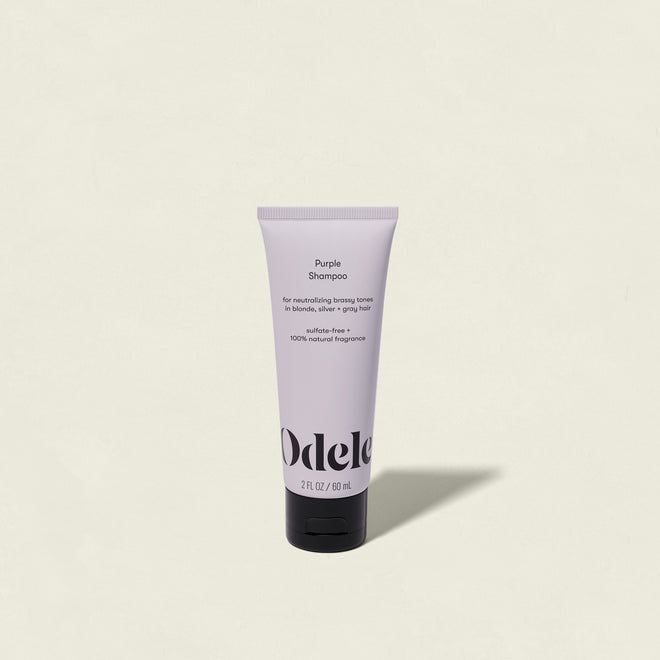 A tube of Purple Shampoo Mini stands upright against a plain, off-white background. This lavender-colored shampoo is designed for blonde hair, helping to neutralize brassy tones and create a brighter appearance.