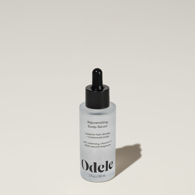 A bottle of Odele Rejuvenating Scalp Serum stands upright against a plain, light-colored backdrop with the front of the label facing the camera.