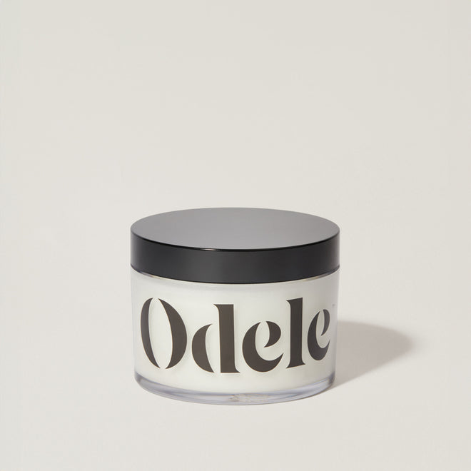 A jar of Odele Scalp & Body Scrub stands upright against a plain, light-colored backdrop with the front of the label facing the camera.