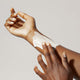 A person with medium brown skin applies Odele Scalp & Body Scrub to their forearm with their fingers against a plain, light background.