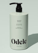 A light green bottle of Odele Smoothing Shampoo Bulk with a black pump, featuring benefits like extra moisture, frizz control, shine, sulfate-free formula, and natural fragrance, set against a pale green background.