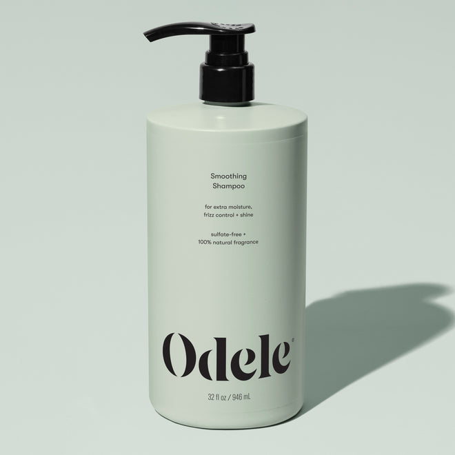 A light green bottle of Odele Smoothing Shampoo Bulk with a black pump, featuring benefits like extra moisture, frizz control, shine, sulfate-free formula, and natural fragrance, set against a pale green background.
