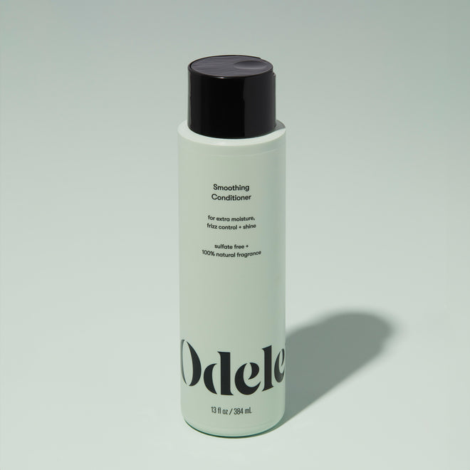 A bottle of Odele Smoothing Conditioner stands upright against a plain light green backdrop with the front of the label facing the camera.