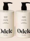 Two bottles of Odele Smoothing Shampoo and Conditioner stands upright against a plain, light-colored backdrop with the front of the label facing the camera.