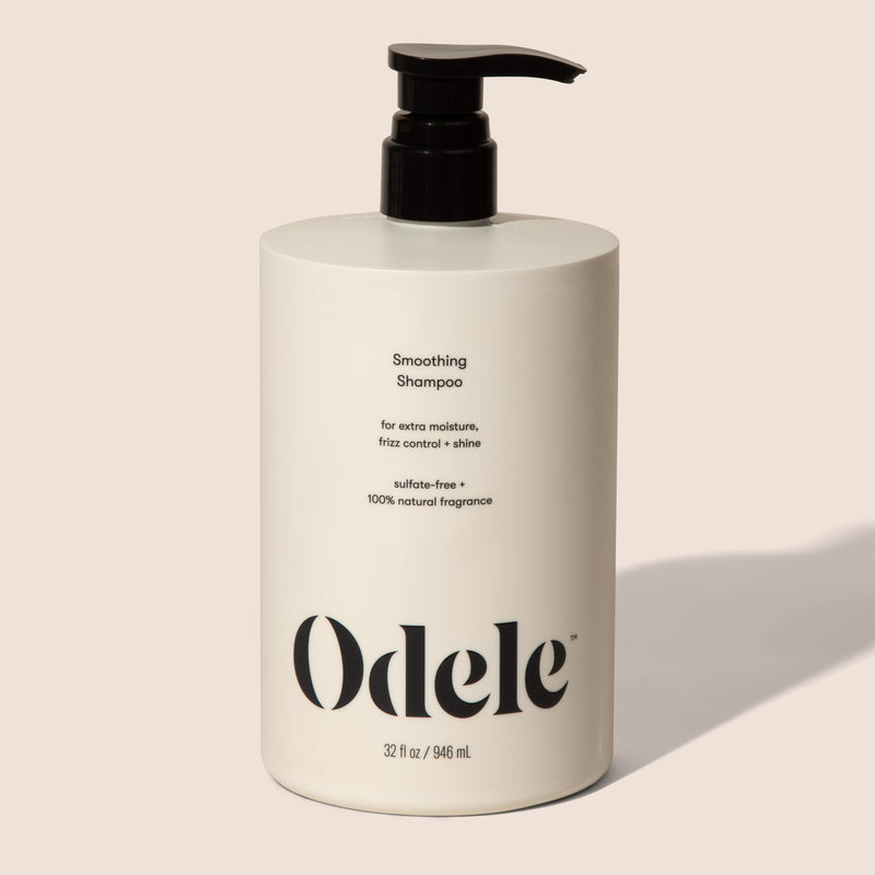 A bottle of Odele Smoothing Shampoo stands upright against a plain light colored backdrop with the front of the label facing the camera.