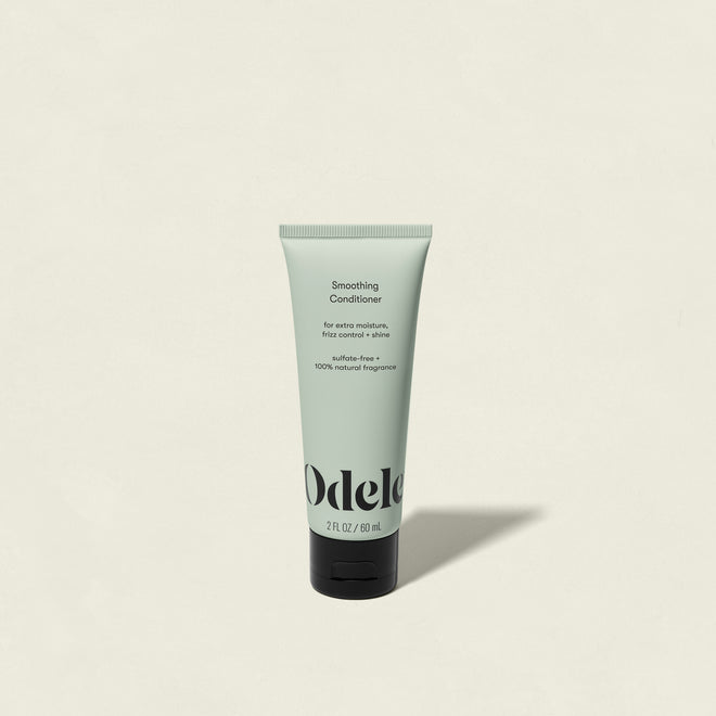 A light green tube of Smoothing Conditioner Mini stands upright on a plain off-white background, featuring black text and a black flip-top cap—this salon-grade conditioner provides shine and frizz control.