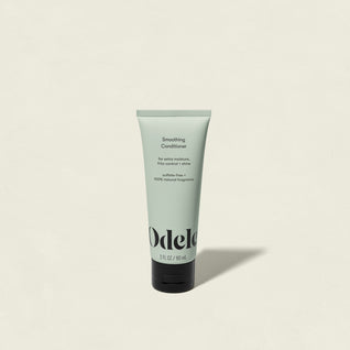 A light green tube of Smoothing Conditioner Mini stands upright on a plain off-white background, featuring black text and a black flip-top cap—this salon-grade conditioner provides shine and frizz control.