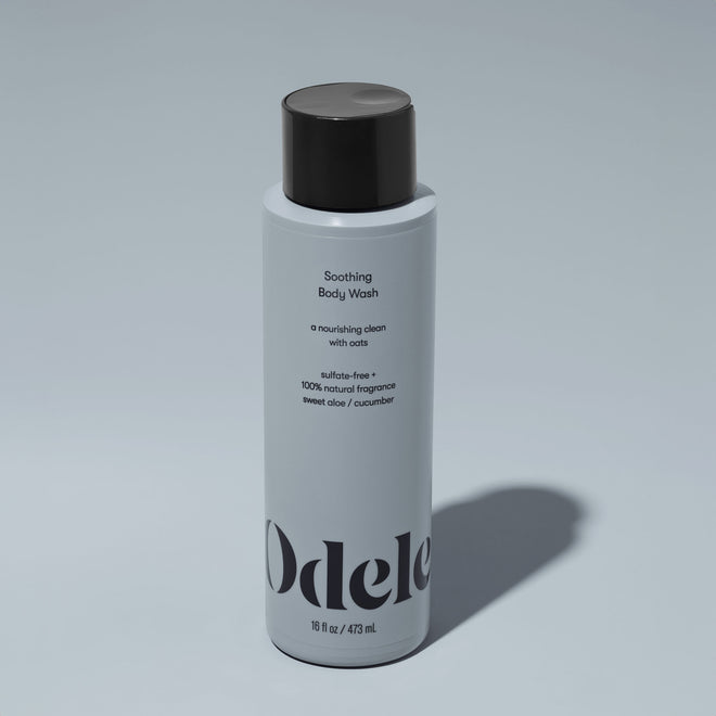 A bottle of Odele Soothing Body Wash stands upright against a plain light blue backdrop with the front of the label facing the camera.