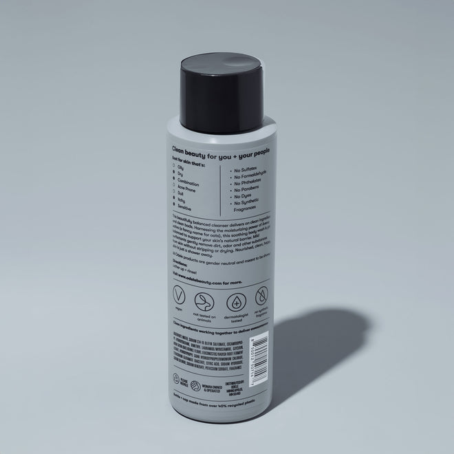 A bottle of Odele Soothing Body Wash stands upright against a plain light blue backdrop with the back of the label facing the camera.